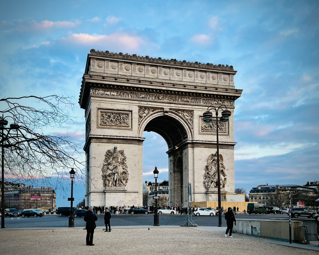 A striking view of the Arc de Triomphe in Paris, with its intricate carvings and grand arch standing tall against a blue evening sky.