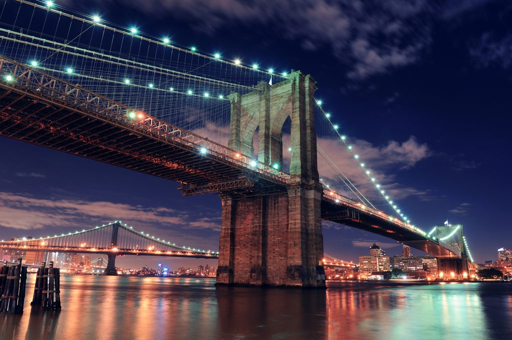 Brooklyn Bridge closeup over East River at night in New York City Manhattan with lights and reflections.