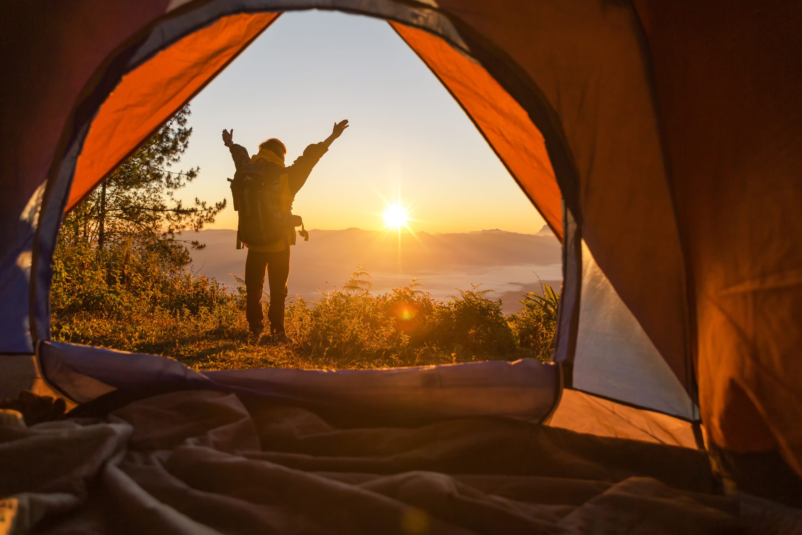 Hiker stand at the camping front orange tent and backpack in the mountains. Backpacker looking into the distance