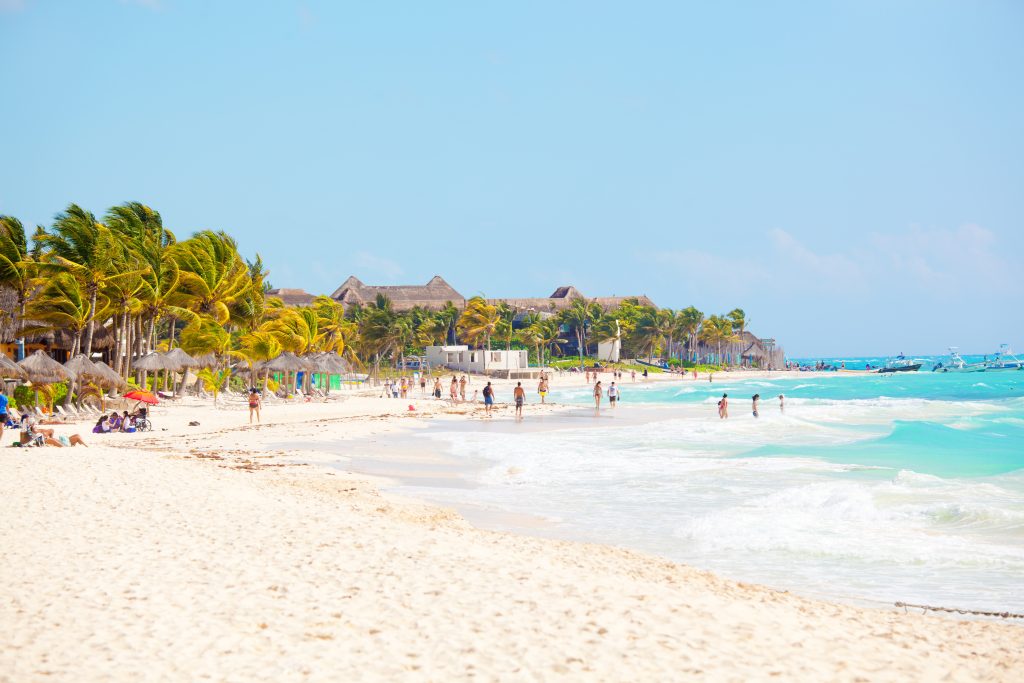 Subject: Vacationing tourists enjoying the beachfront water and white sand of Playa del Carmen along the Caribbean sea, in the Riviera Maya.