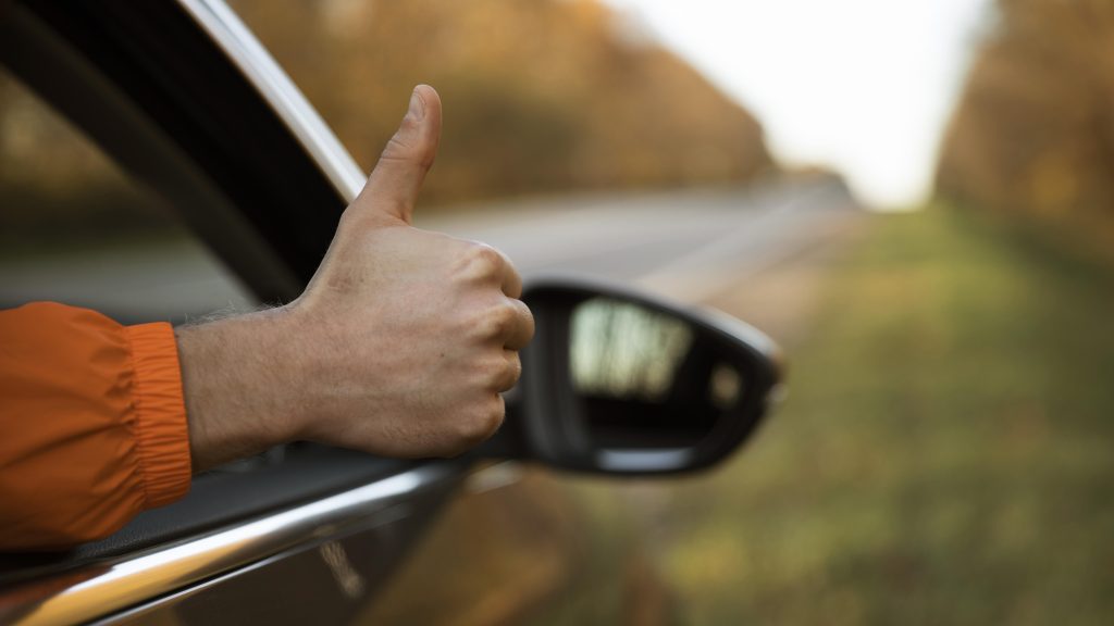 Man giving thumbs up out of his car while on a road trip 