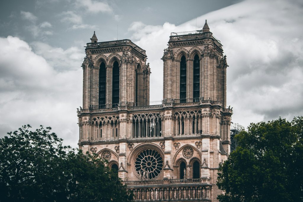 A dramatic view of the iconic Notre Dame Cathedral in Paris, showcasing its Gothic architecture with twin towers framed against a cloudy sky.