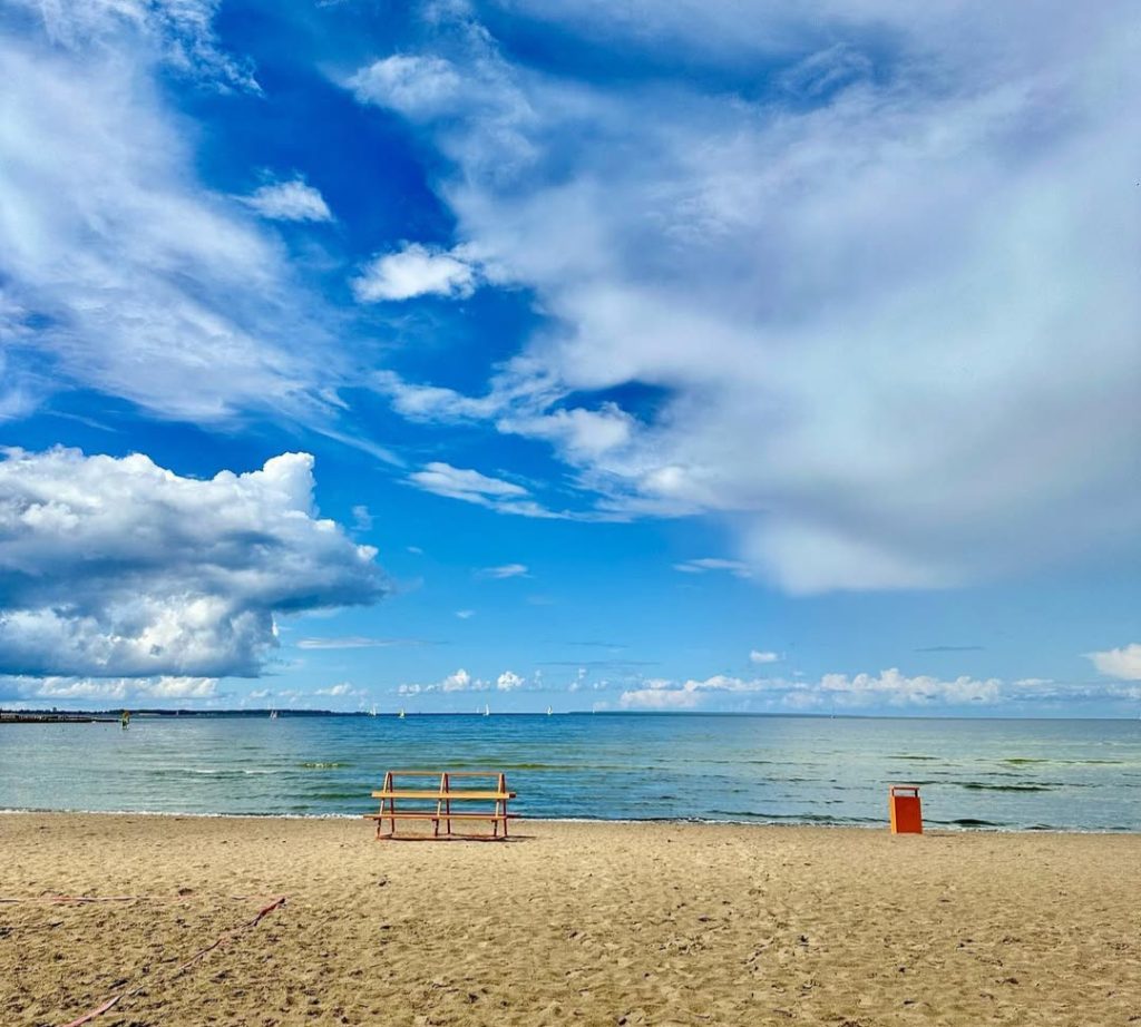 A peaceful view of Pirita Beach in Tallinn, Estonia, with calm waters, a sandy shoreline, and a vibrant blue sky filled with clouds.