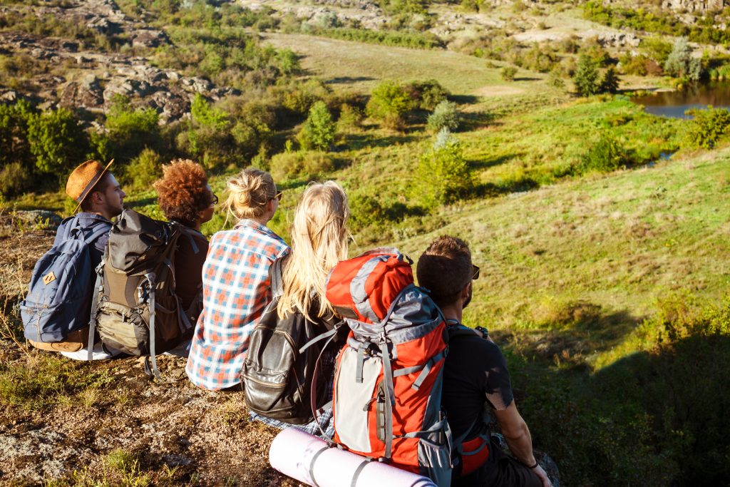 Young beautiful friends travelers with backpacks sitting on rock in canyon, enjoying view. 